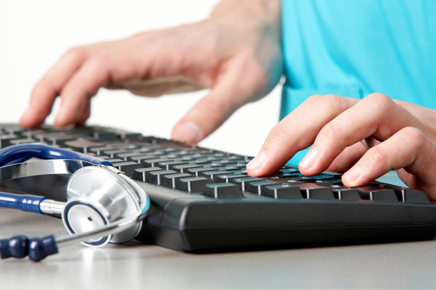 Hand entering data on a computer keyboard in a medical setting.