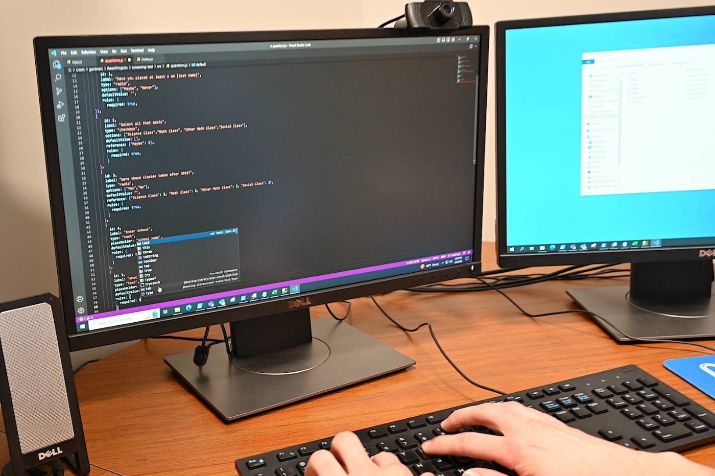 Student at desk using keyboard to write software code displayed on computer monitor